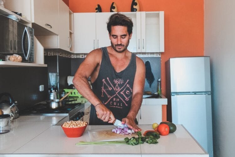 man wearing a singlet cutting fruit and vegetables for lunch