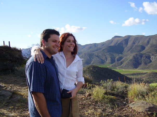A smiling young man and woman standing on a hill overlooking a valley