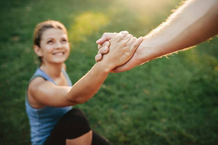 Close up shot of man helping woman to stand up. Focus on hands of couple exercising at park.