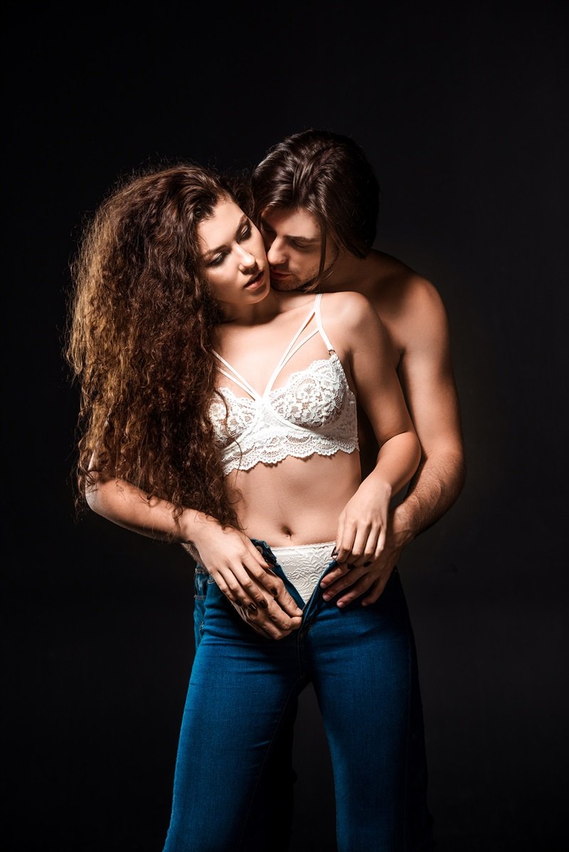 portrait of man taking off girlfriends jeans isolated on black sexual tension