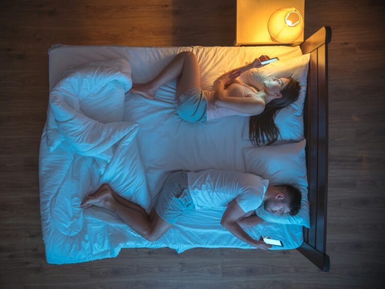 The unhappy couple with smartphone lay on the bed. night time. view from above.