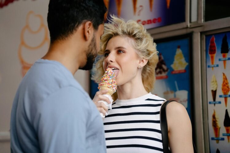 Woman with tousled hair licking an ice cream and looking in mans eyes