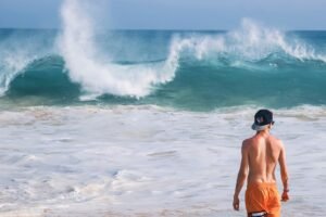 man in orange shorts standing near wavy sea during daytime
