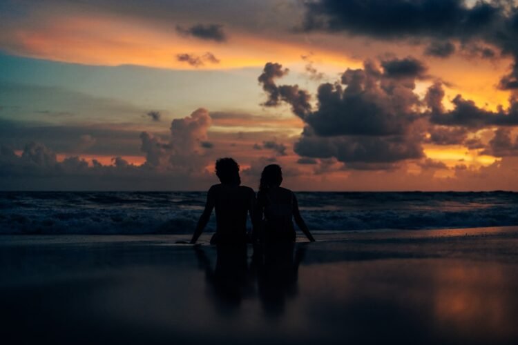 Two people standing on a beach at sunset
