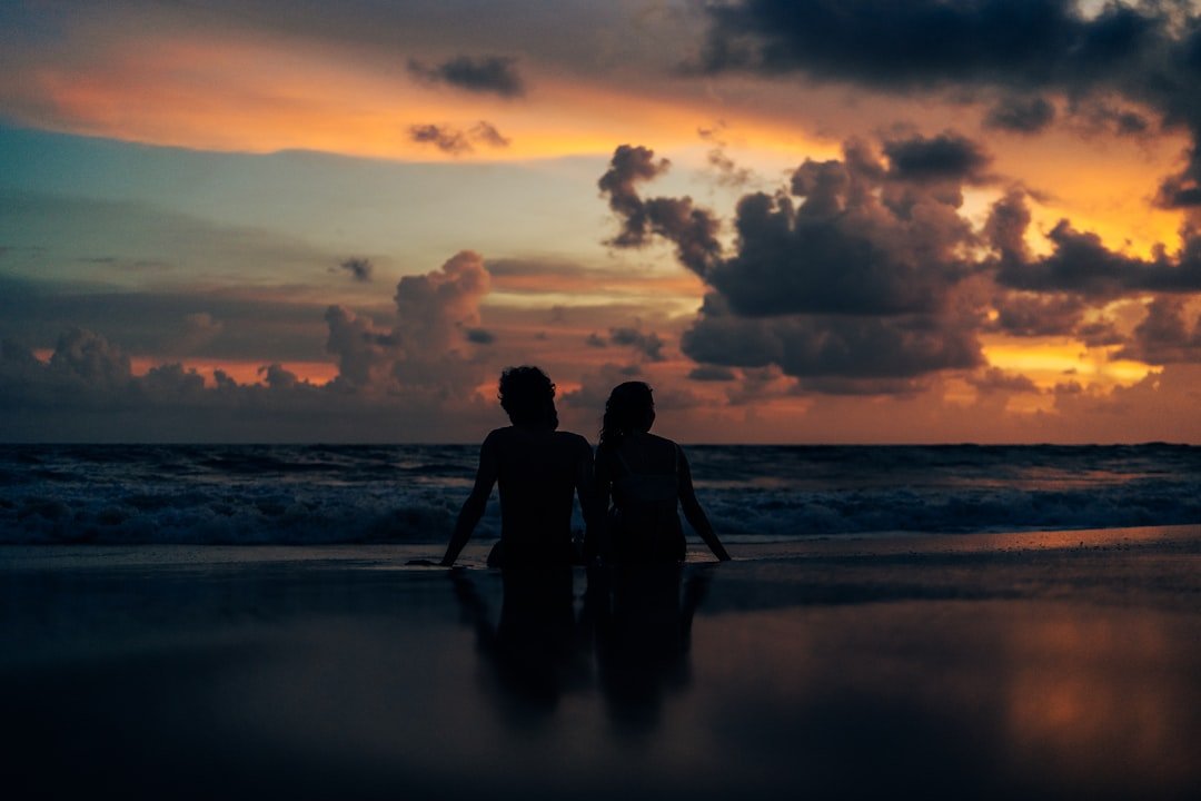 Two people standing on a beach at sunset