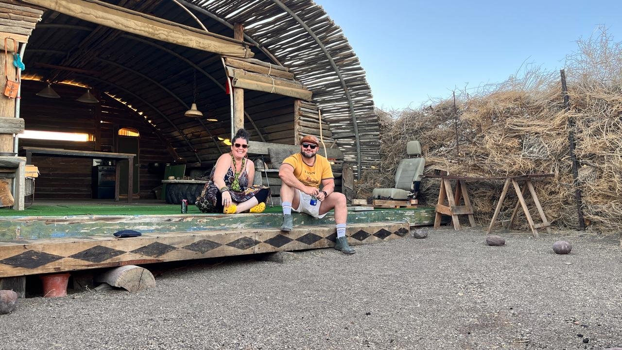 Two people sitting outside a hut.